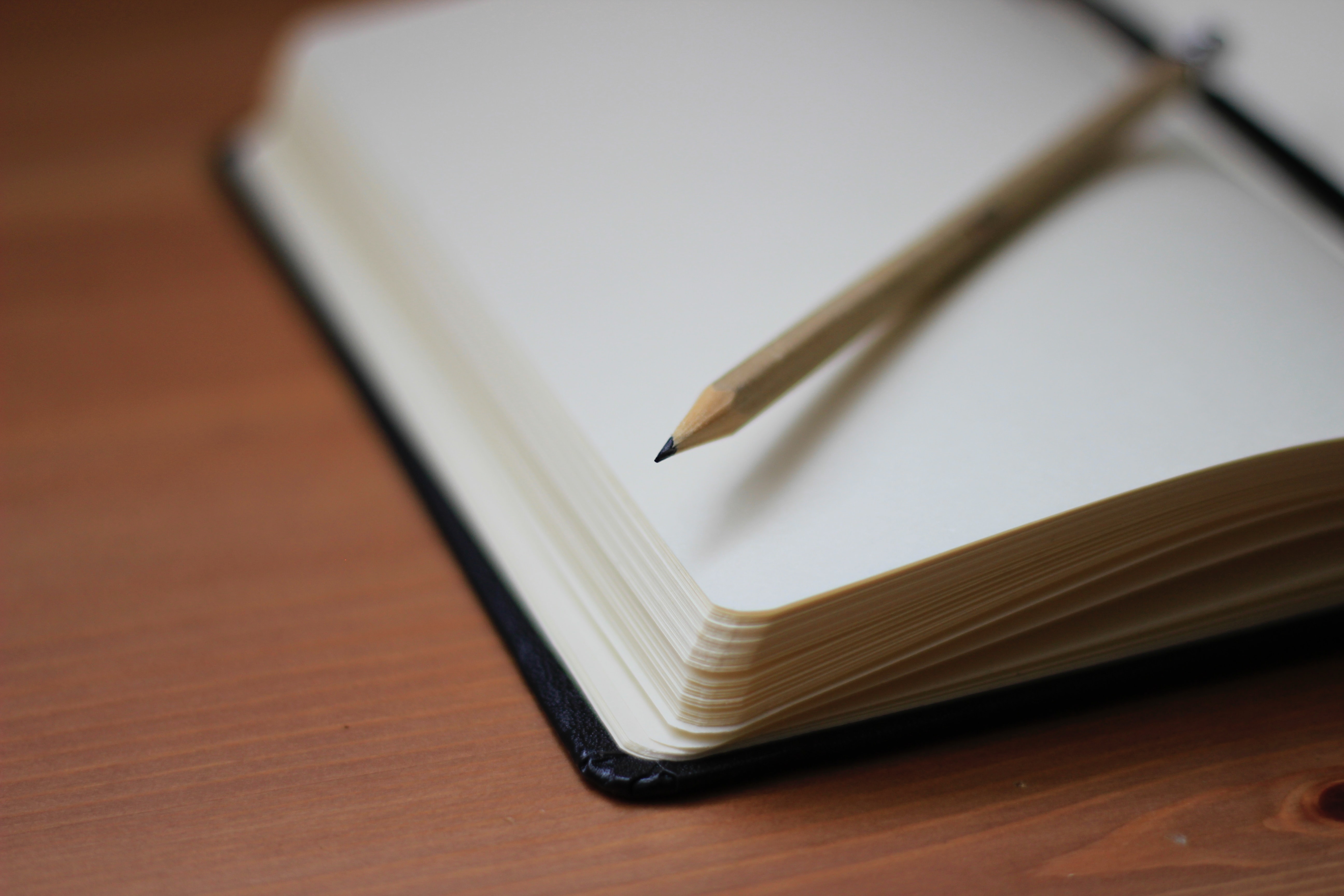 An open blank notebook and a pencil resting on a wooden table.