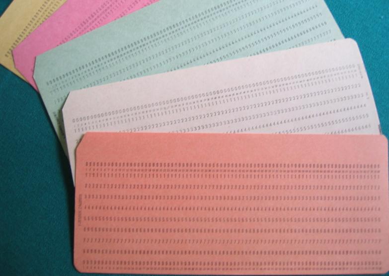 A fan of pink, green, and cream punched cards with rows of printed numbers.
